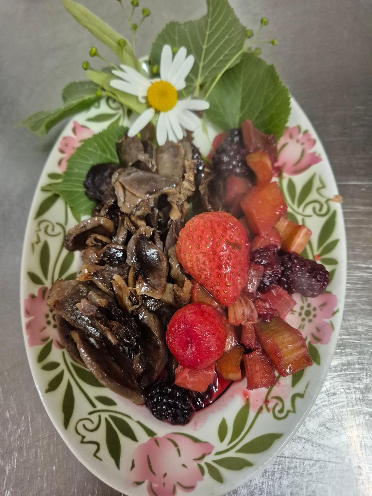 Une assiette de champignons et de fruits rouges, fraises et mûres, décorée d’une marguerite.