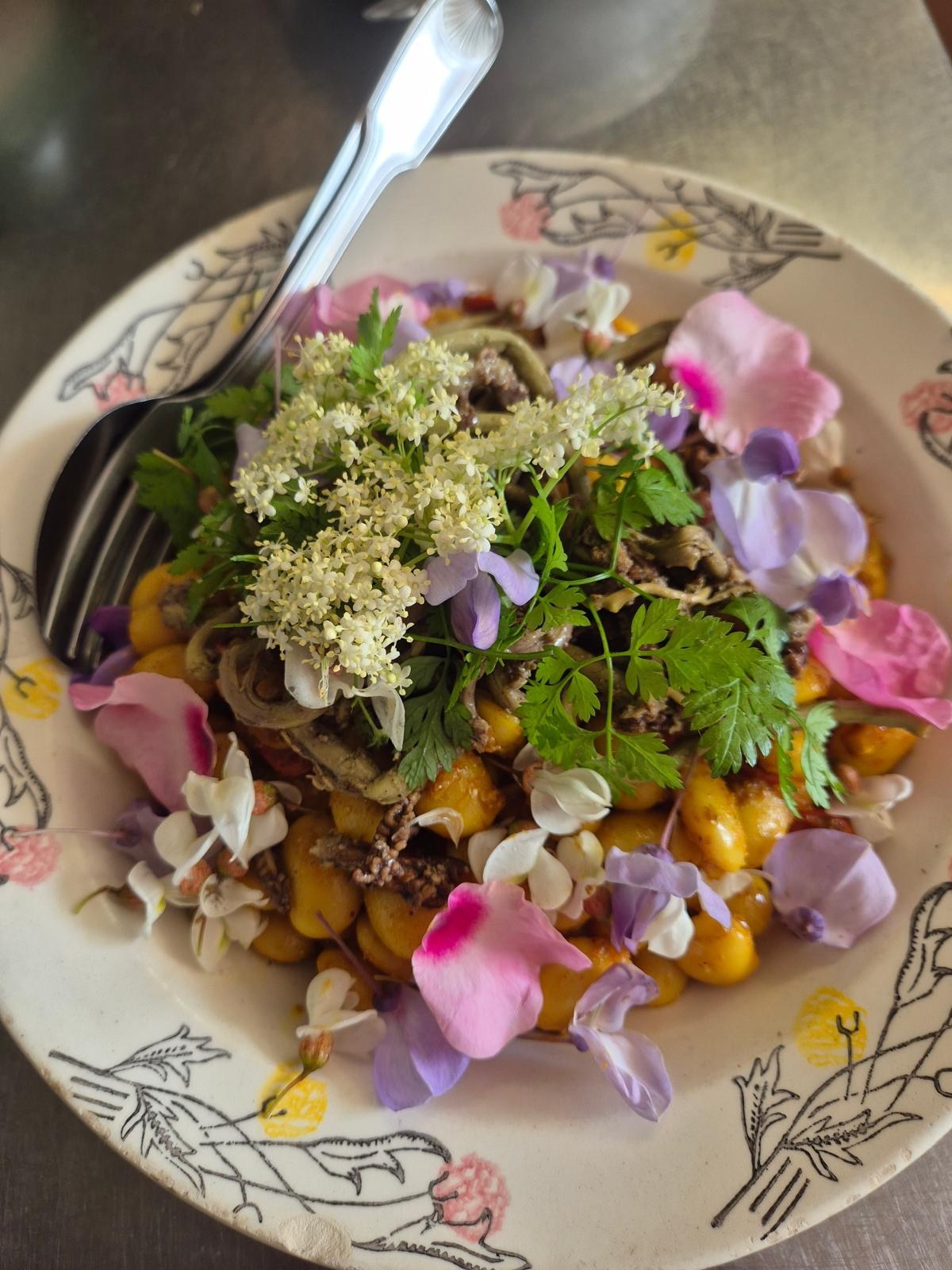 Une assiette de pommes de terre recouverte de fleurs de sureau, de pétales roses et mauves et d’herbes du jardin.