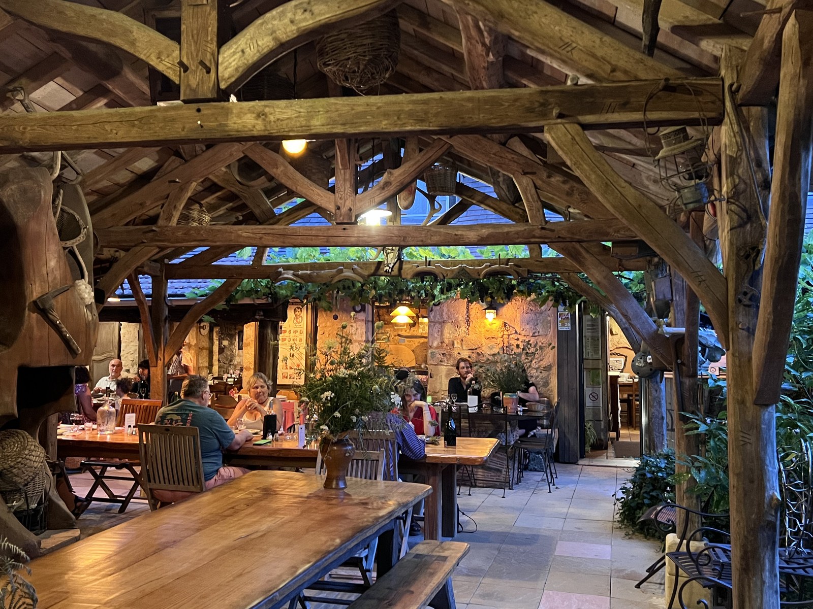 Des convives attablés sous la charpente de l’auberge, un soir d’été.