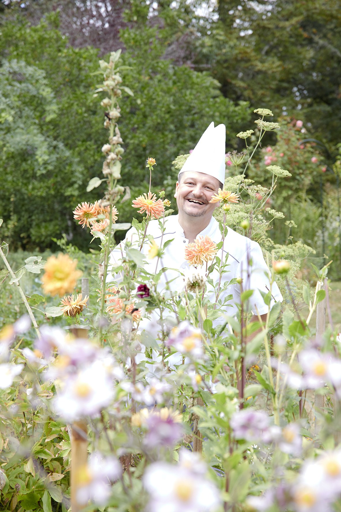 Régis Gagnadre, en toque, riant au milieu des dahlias du jardin.