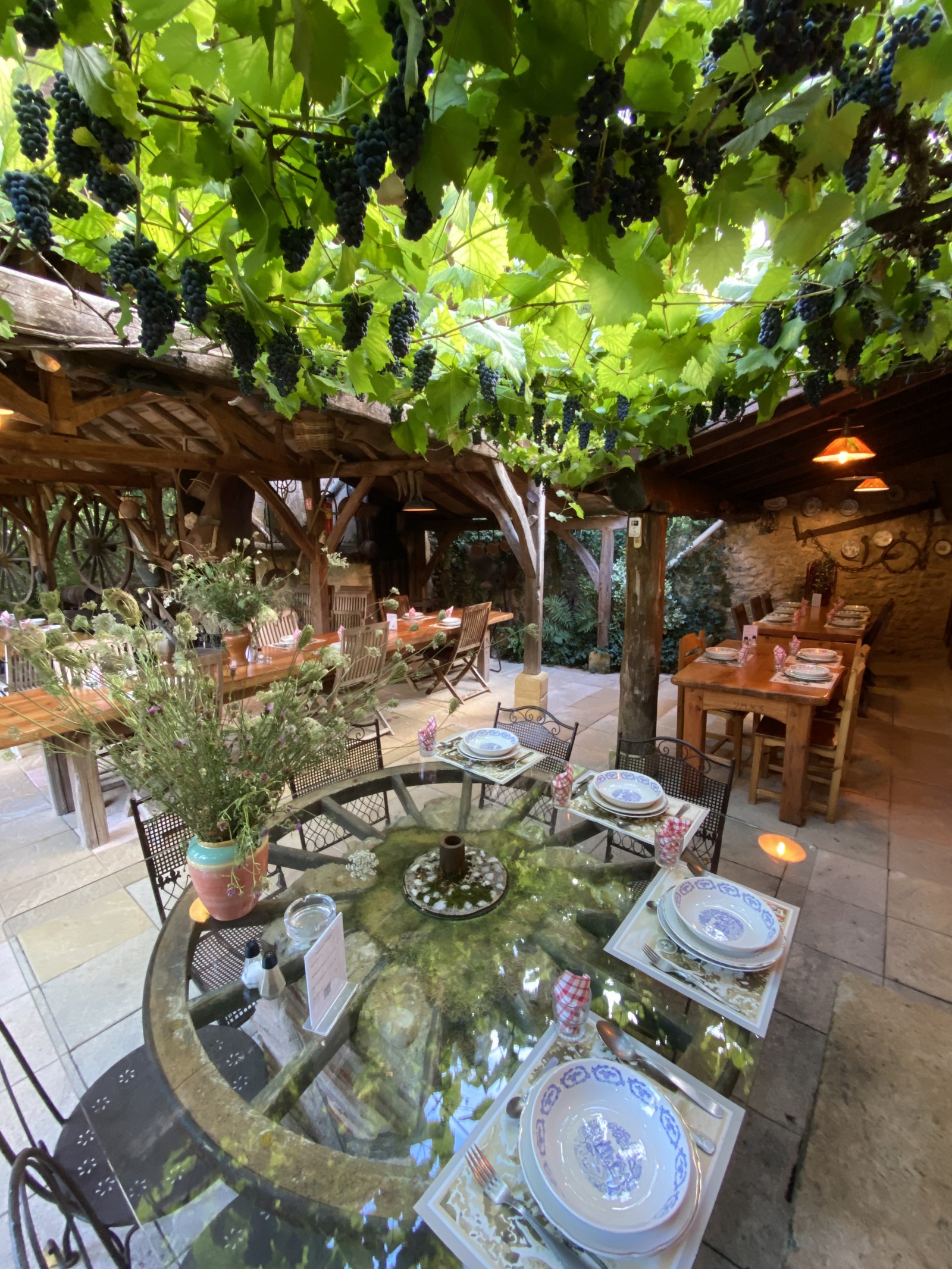 La terrasse dans sa longueur, la roue de charrette et les tables.